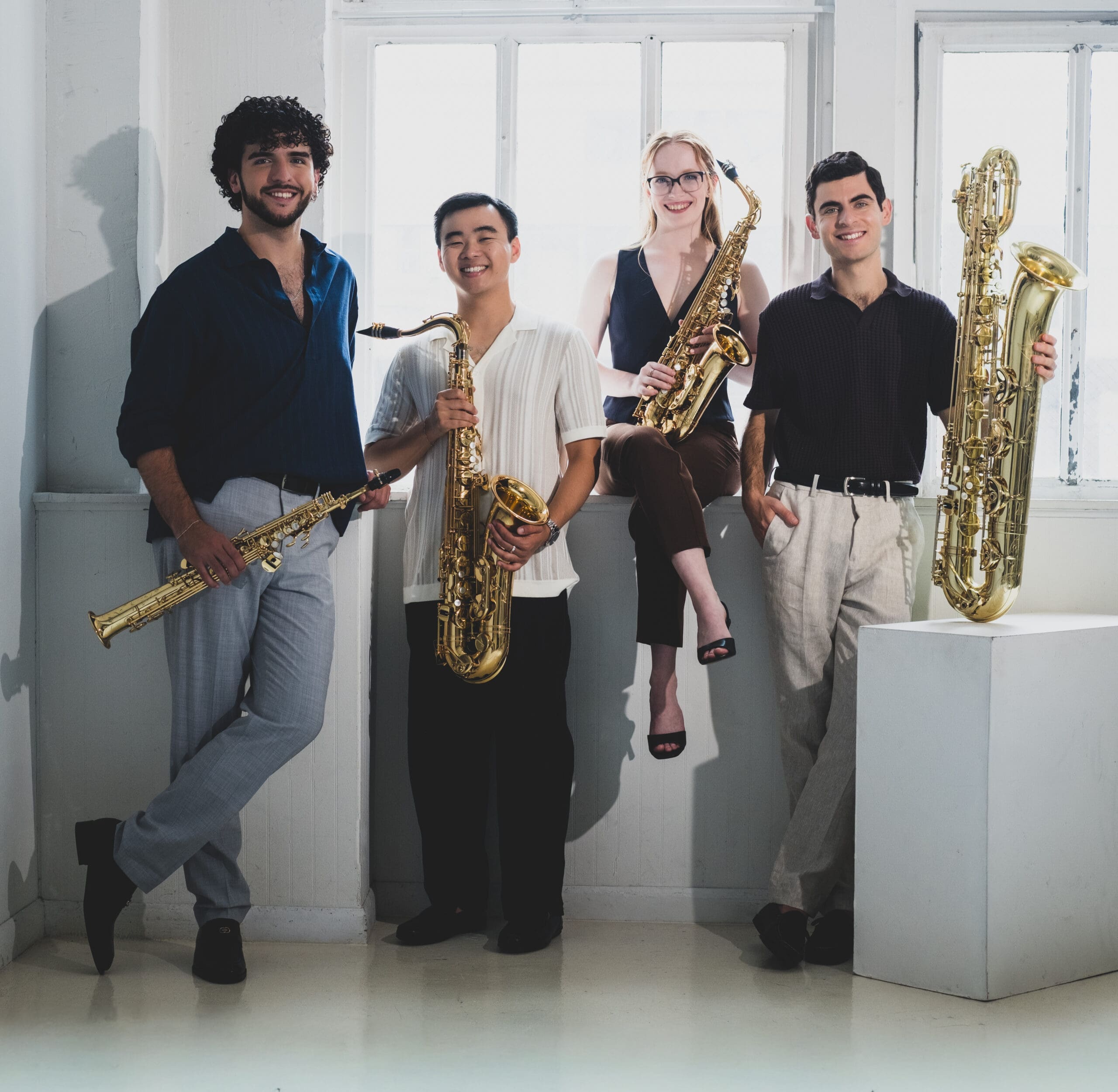 Four musicians posing with their saxophones in a bright, white studio setting.